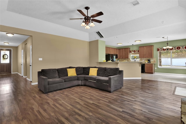 living room featuring ceiling fan with notable chandelier, a tray ceiling, hardwood / wood-style flooring, and a healthy amount of sunlight