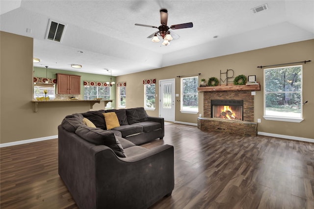 living room with ceiling fan, dark hardwood / wood-style flooring, a textured ceiling, and a stone fireplace