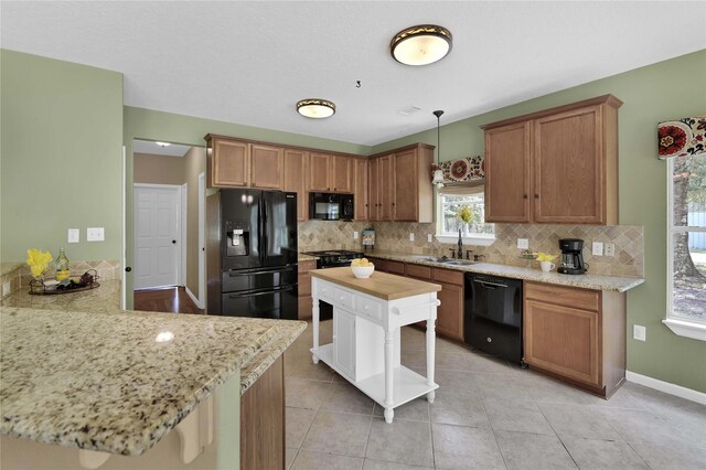 kitchen with a breakfast bar area, light tile patterned floors, hanging light fixtures, backsplash, and black appliances