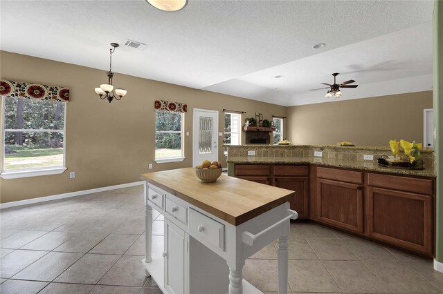 kitchen with light tile patterned flooring, butcher block countertops, ceiling fan with notable chandelier, and pendant lighting