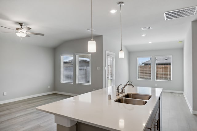 kitchen with sink, decorative light fixtures, vaulted ceiling, light hardwood / wood-style flooring, and an island with sink