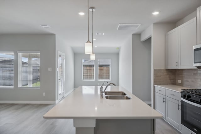 kitchen featuring decorative light fixtures, tasteful backsplash, sink, stainless steel appliances, and a center island with sink