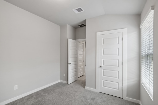 unfurnished bedroom featuring multiple windows, lofted ceiling, and light carpet