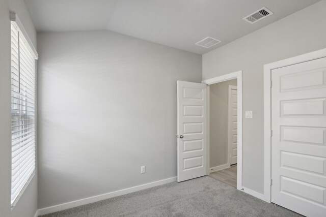 unfurnished bedroom with vaulted ceiling and light carpet