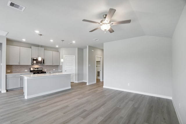 kitchen with decorative light fixtures, a center island with sink, light wood-type flooring, appliances with stainless steel finishes, and backsplash