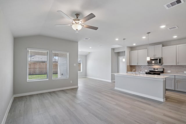 kitchen with appliances with stainless steel finishes, a kitchen island with sink, light hardwood / wood-style floors, decorative backsplash, and decorative light fixtures