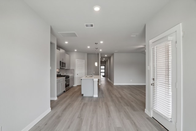 kitchen featuring sink, backsplash, hanging light fixtures, stainless steel appliances, and a center island with sink