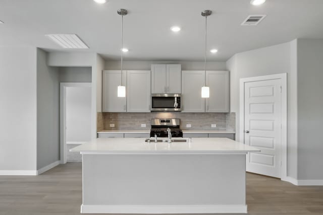 kitchen featuring hanging light fixtures, appliances with stainless steel finishes, a kitchen island with sink, and decorative backsplash