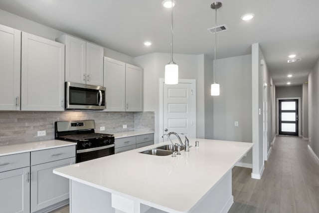 kitchen with sink, backsplash, hanging light fixtures, stainless steel appliances, and a center island with sink