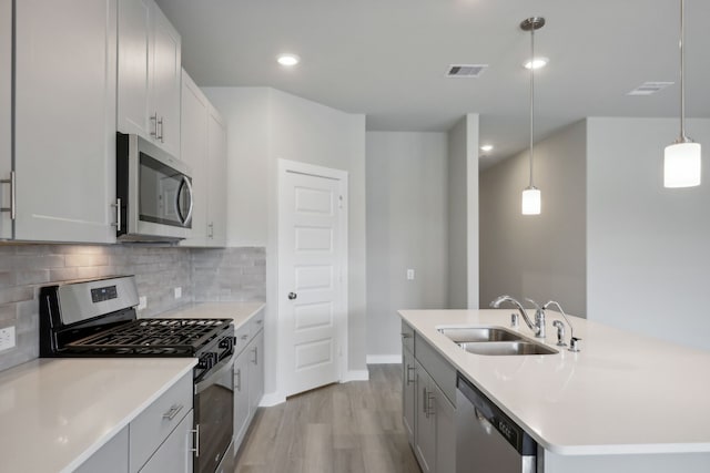 kitchen with decorative light fixtures, tasteful backsplash, sink, stainless steel appliances, and a center island with sink