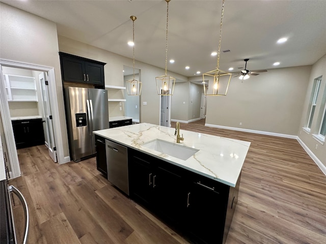 kitchen with pendant lighting, a kitchen island with sink, hardwood / wood-style flooring, stainless steel appliances, and light stone countertops