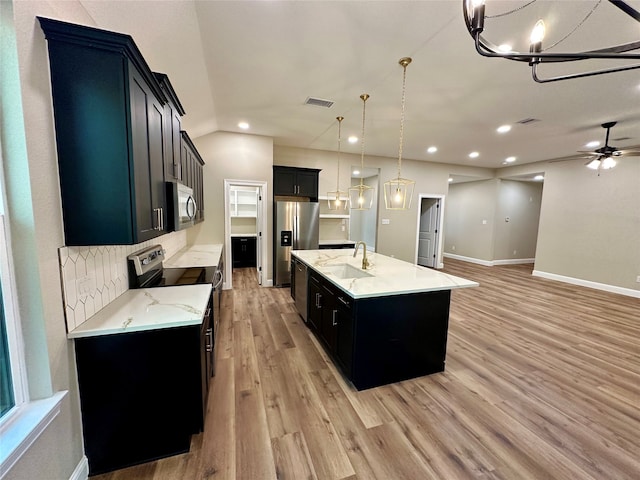 kitchen featuring light wood-type flooring, sink, an island with sink, stainless steel appliances, and decorative light fixtures