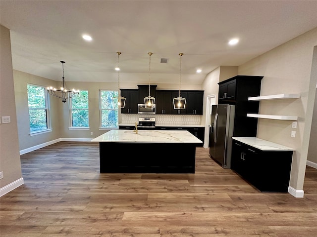 kitchen with light wood-type flooring, a center island with sink, pendant lighting, and stainless steel appliances