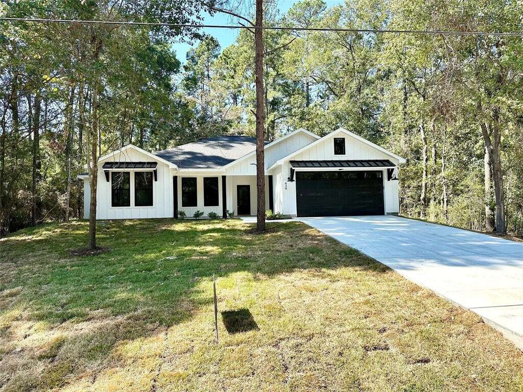 439 Whisperwood Dr, Onalaska, TX 77360 - view of front of property with board and batten siding, an attached garage, driveway, and a front lawn