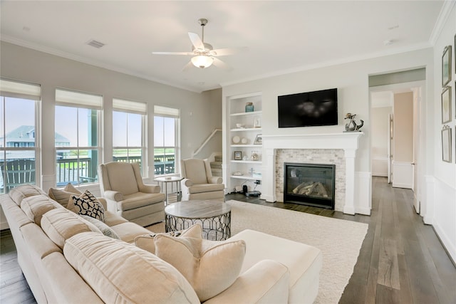 living room with a stone fireplace, crown molding, dark hardwood / wood-style floors, and plenty of natural light