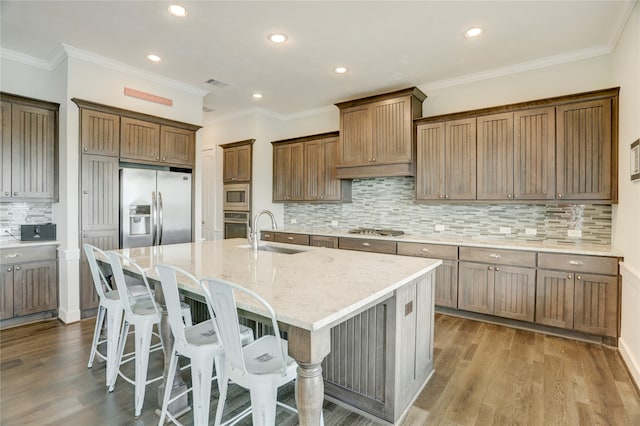 kitchen featuring light hardwood / wood-style floors, stainless steel appliances, sink, a kitchen island with sink, and ornamental molding