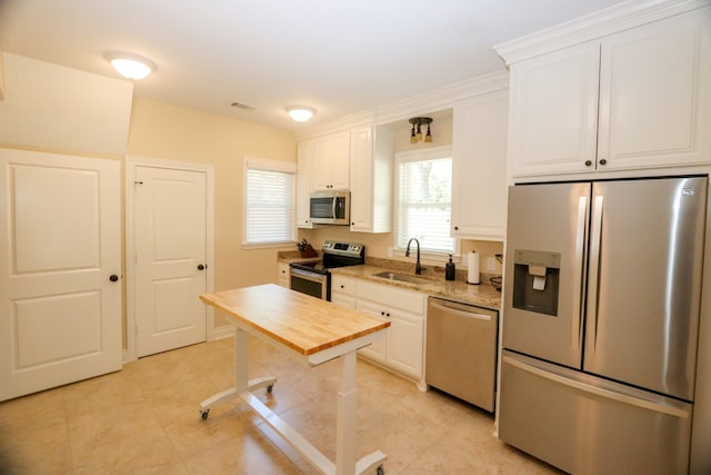 kitchen featuring white cabinetry, sink, light stone countertops, light tile patterned floors, and appliances with stainless steel finishes