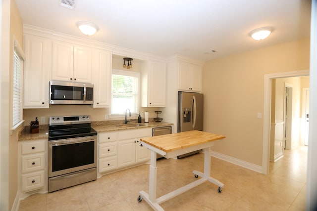 kitchen with sink, stainless steel appliances, light tile patterned floors, light stone counters, and white cabinets