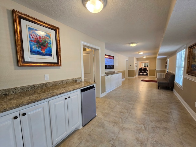 interior space with stainless steel dishwasher, white cabinetry, a textured ceiling, and dark stone counters