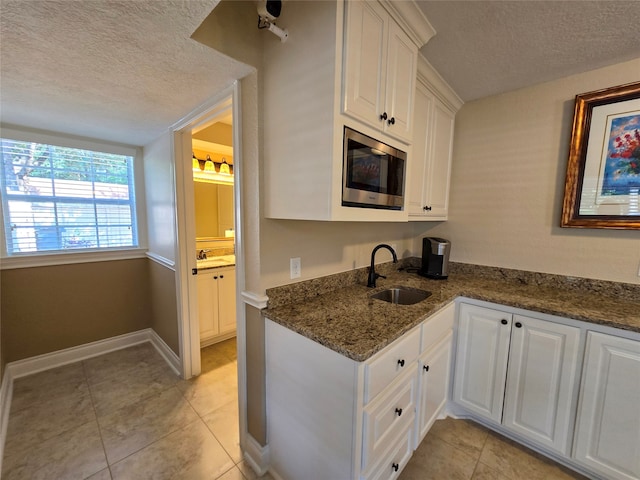 kitchen with dark stone countertops, white cabinetry, stainless steel microwave, and sink