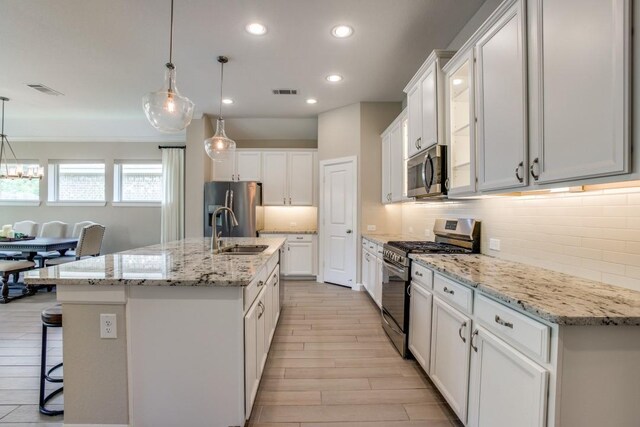 kitchen with decorative backsplash, appliances with stainless steel finishes, white cabinets, a center island with sink, and sink