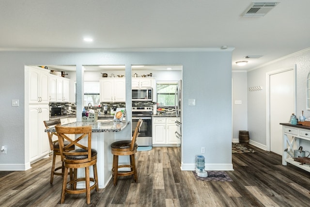 kitchen with tasteful backsplash, stainless steel appliances, white cabinets, dark hardwood / wood-style floors, and a kitchen island