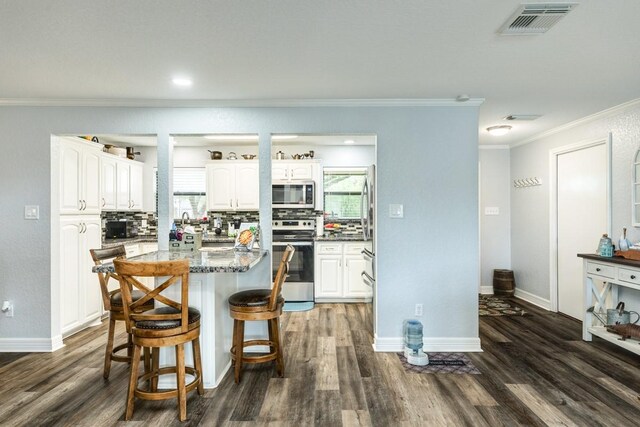 131 Bastrop Bayou Dr, Angleton, TX 77515 - kitchen with ornamental molding, a kitchen bar, stainless steel appliances, white cabinets, and dark wood-style floors