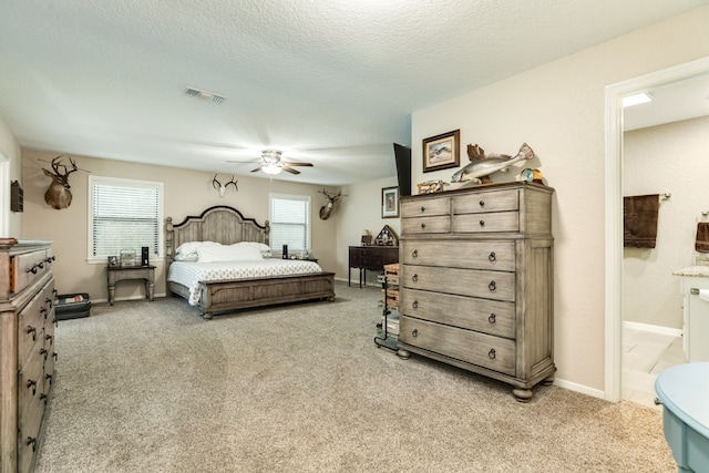 bedroom featuring ceiling fan, a textured ceiling, ensuite bathroom, and light carpet