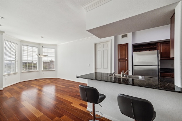 kitchen featuring sink, dark wood-type flooring, kitchen peninsula, stainless steel fridge, and pendant lighting