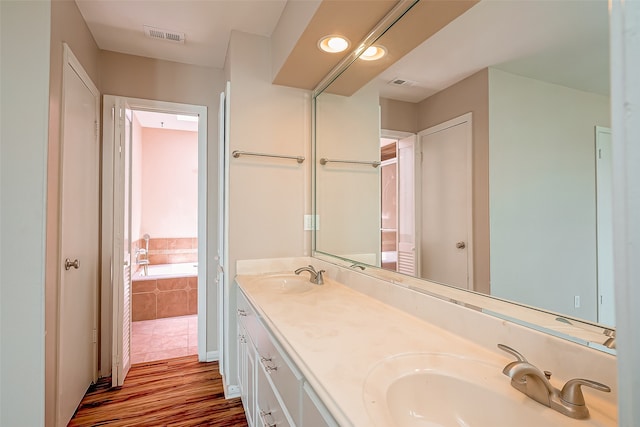 bathroom featuring wood-type flooring, tiled bath, and vanity