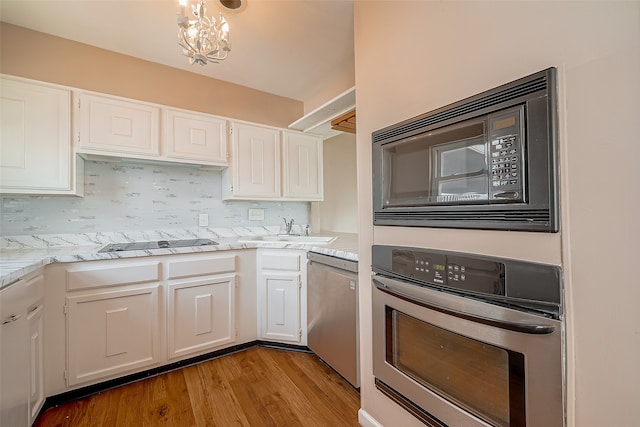 kitchen with an inviting chandelier, white cabinets, black appliances, and light hardwood / wood-style floors