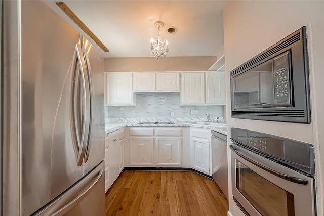 kitchen featuring white cabinets, backsplash, a chandelier, black appliances, and light wood-type flooring