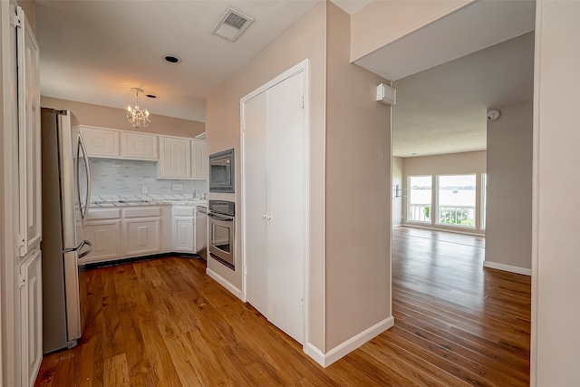 kitchen featuring light hardwood / wood-style floors, tasteful backsplash, white cabinets, stainless steel appliances, and a notable chandelier