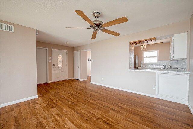 unfurnished living room featuring ceiling fan, light wood-type flooring, and sink