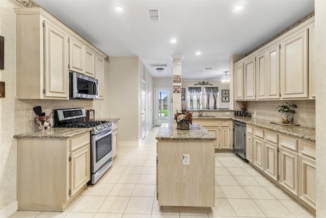 kitchen featuring light stone countertops, sink, a center island, light tile patterned floors, and appliances with stainless steel finishes