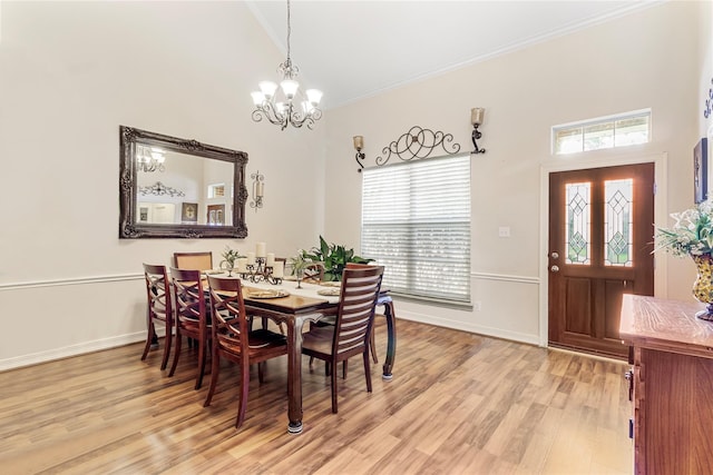 dining space with a towering ceiling, light wood-type flooring, an inviting chandelier, and ornamental molding