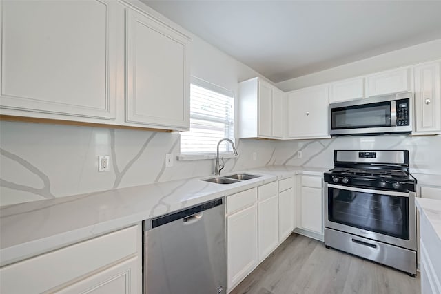 kitchen featuring sink, light stone countertops, light hardwood / wood-style floors, white cabinetry, and stainless steel appliances