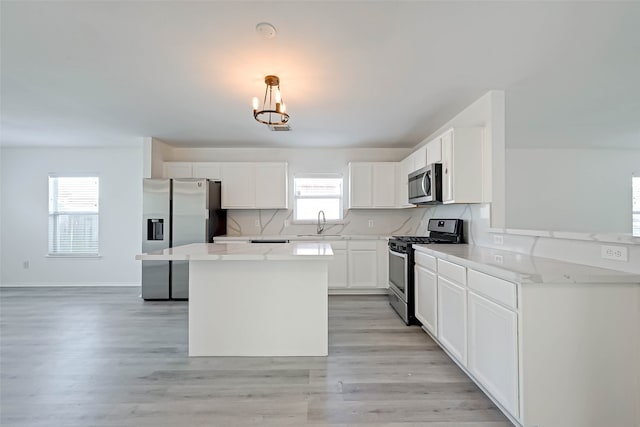 kitchen with a wealth of natural light, white cabinets, hanging light fixtures, and appliances with stainless steel finishes