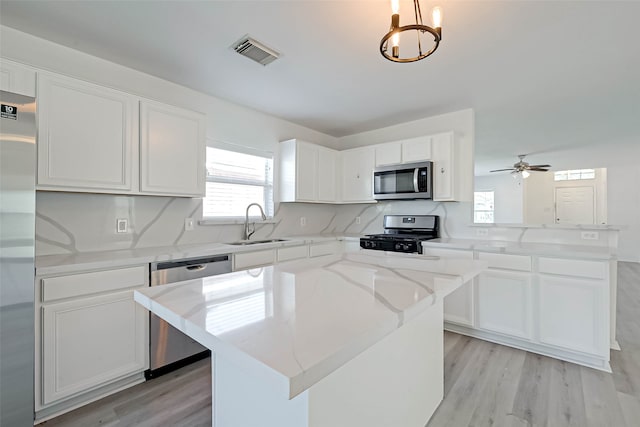 kitchen with white cabinets, a kitchen island, hanging light fixtures, and appliances with stainless steel finishes