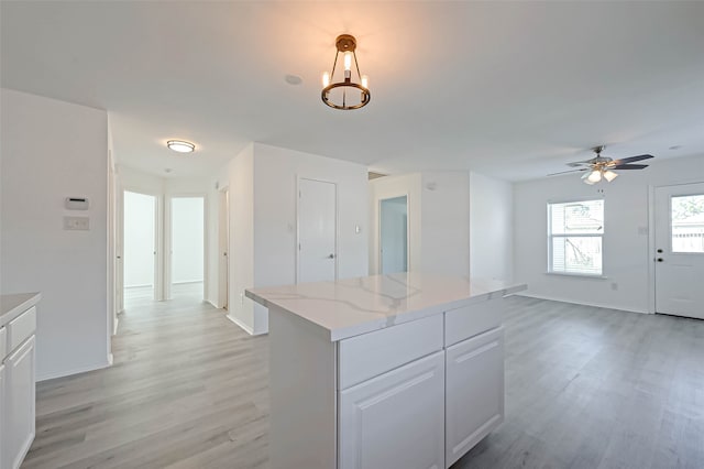 kitchen with light stone countertops, ceiling fan with notable chandelier, light hardwood / wood-style flooring, white cabinets, and hanging light fixtures