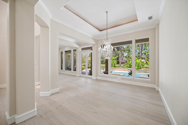 unfurnished dining area featuring a notable chandelier, a tray ceiling, light wood-type flooring, and ornamental molding