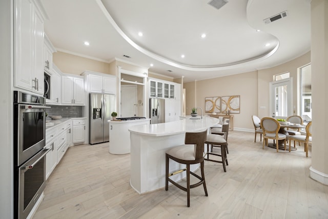 kitchen featuring a tray ceiling, an island with sink, white cabinets, light hardwood / wood-style flooring, and appliances with stainless steel finishes