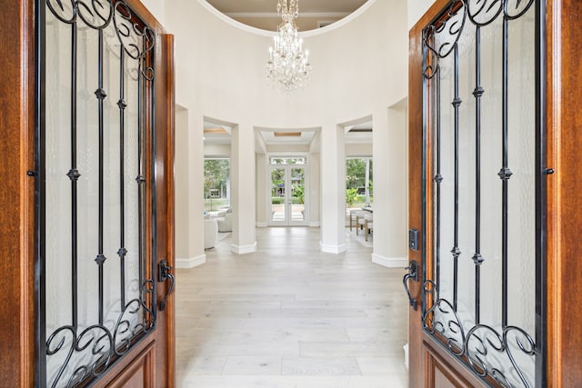 foyer with an inviting chandelier, light hardwood / wood-style flooring, a towering ceiling, and decorative columns