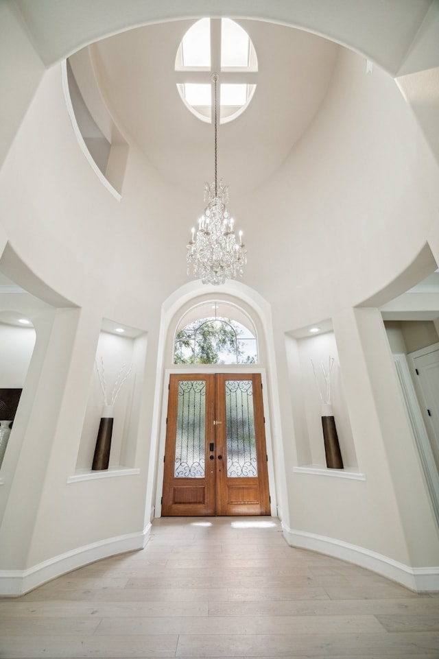 entryway featuring french doors, light wood-type flooring, a chandelier, and a high ceiling