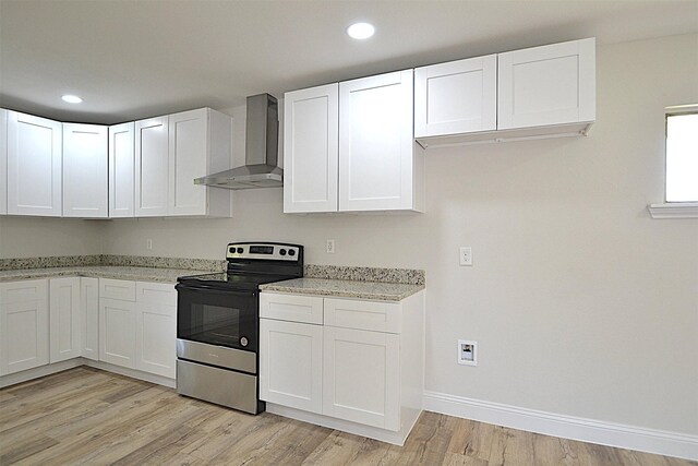 kitchen with light hardwood / wood-style flooring, stainless steel range with electric stovetop, wall chimney exhaust hood, and white cabinets