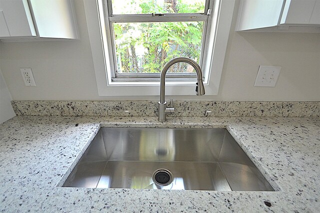 room details featuring light stone counters, sink, and white cabinetry