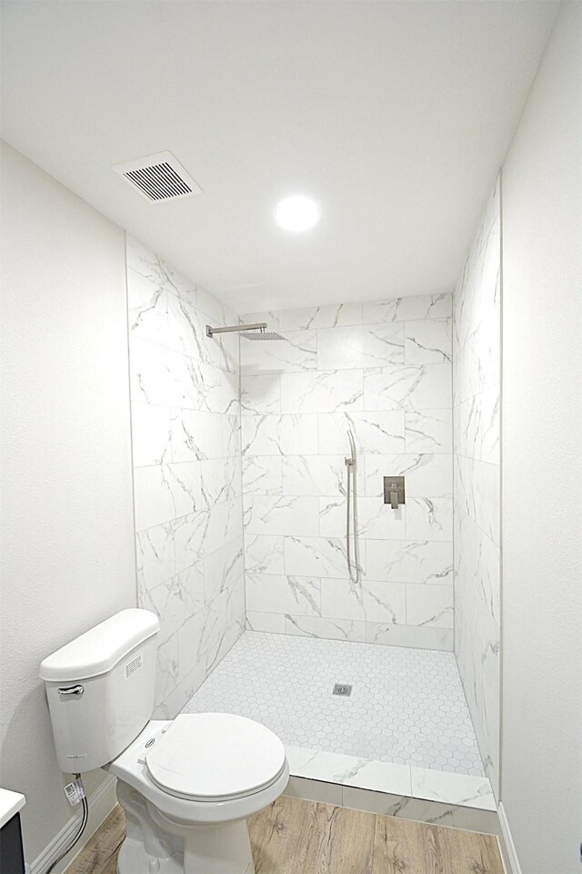 bathroom with tiled shower, toilet, vanity, and wood-type flooring