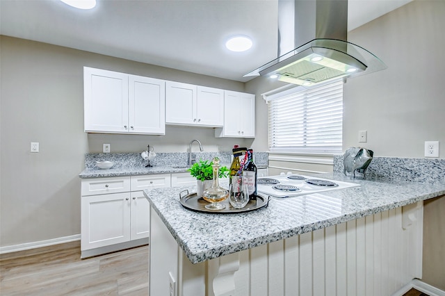 kitchen with a breakfast bar area, island exhaust hood, light stone countertops, white cabinetry, and light hardwood / wood-style flooring