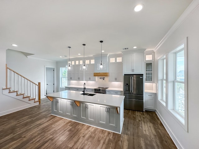 kitchen featuring a center island with sink, sink, ornamental molding, stainless steel fridge, and dark hardwood / wood-style floors