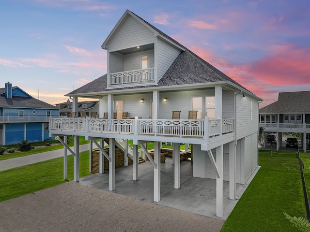 back house at dusk featuring a yard, a garage, and a balcony